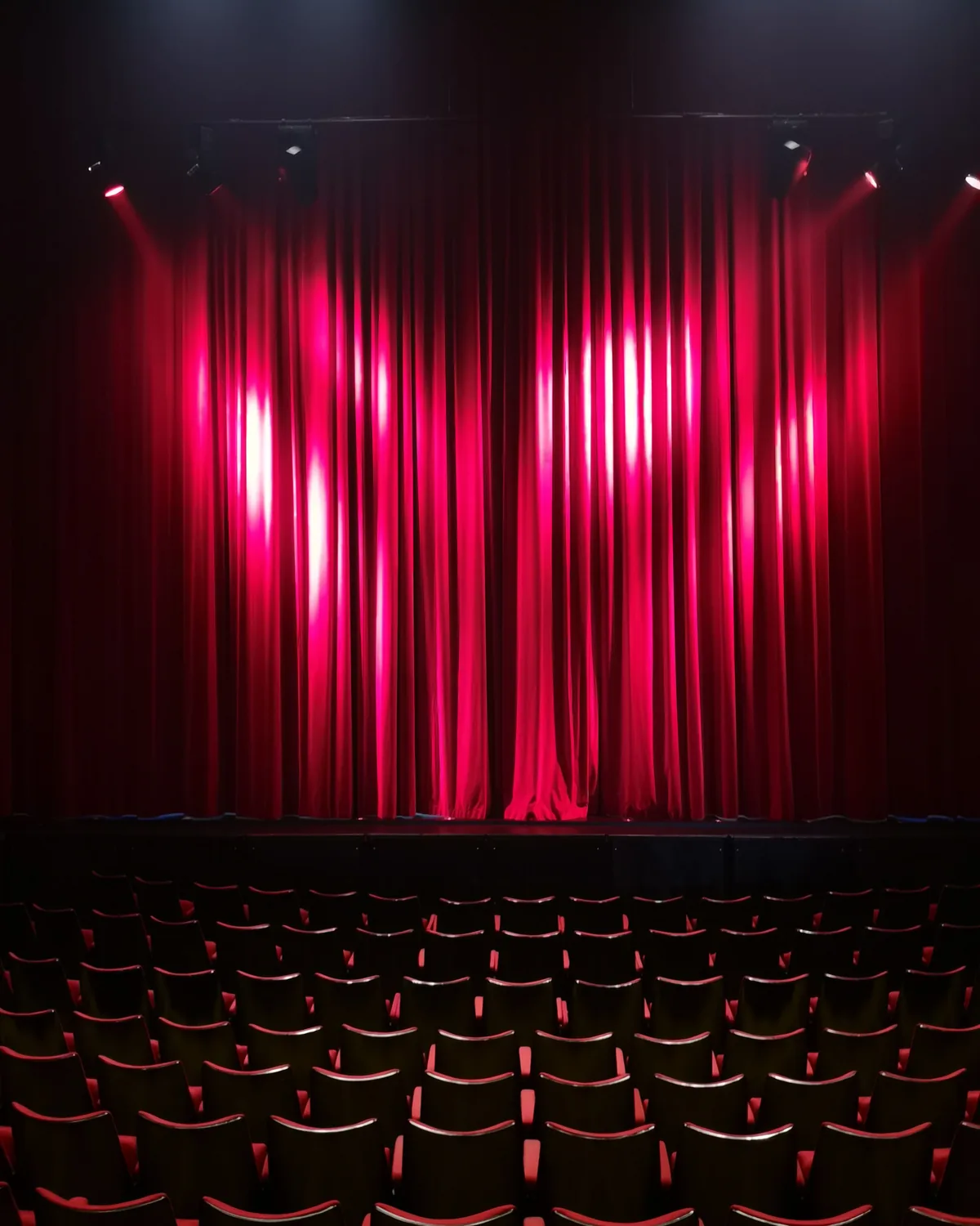 A red stage curtain lit above rows of empty theatre seats